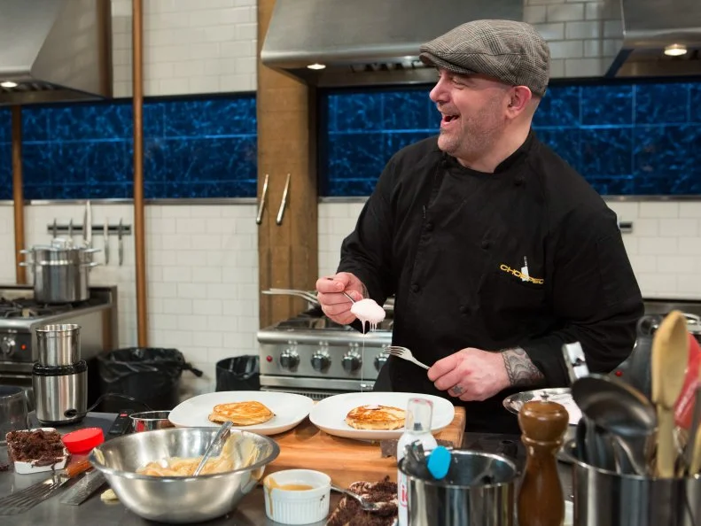 Chef Chris Santos jokes with the other chefs while he works with the ingredients from the "short order" episode: banana pudding, vanilla ice cream, icing, brownie mix, as seen on Food Network's Chopped After Hours, Season 21.