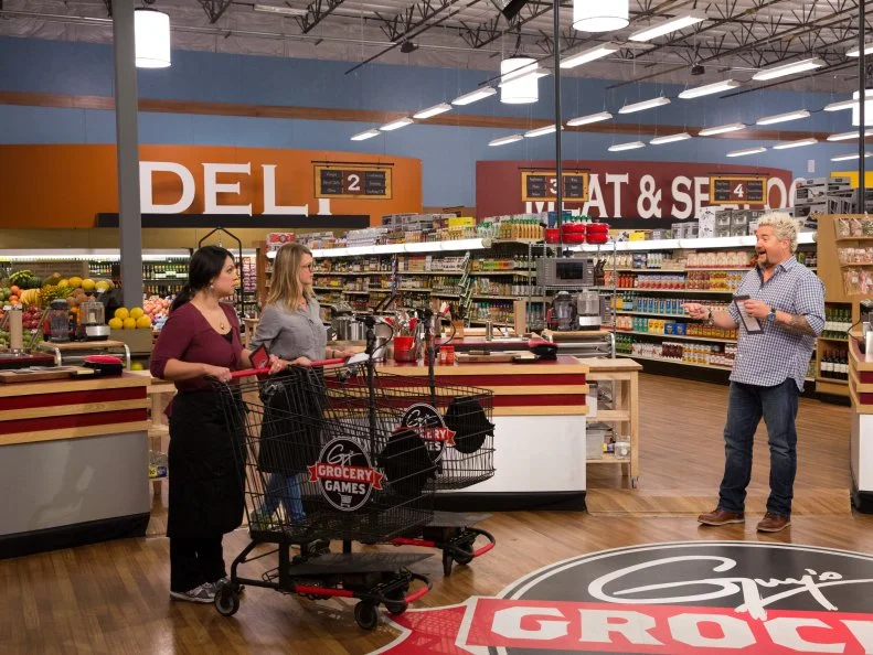 Host Guy Fieri prepares Chefs Veronica Eiken and Erika Tucker to shop during Game 3, Flip This Dish, as seen on Food Network's Guy's Grocery Games, Season 7.