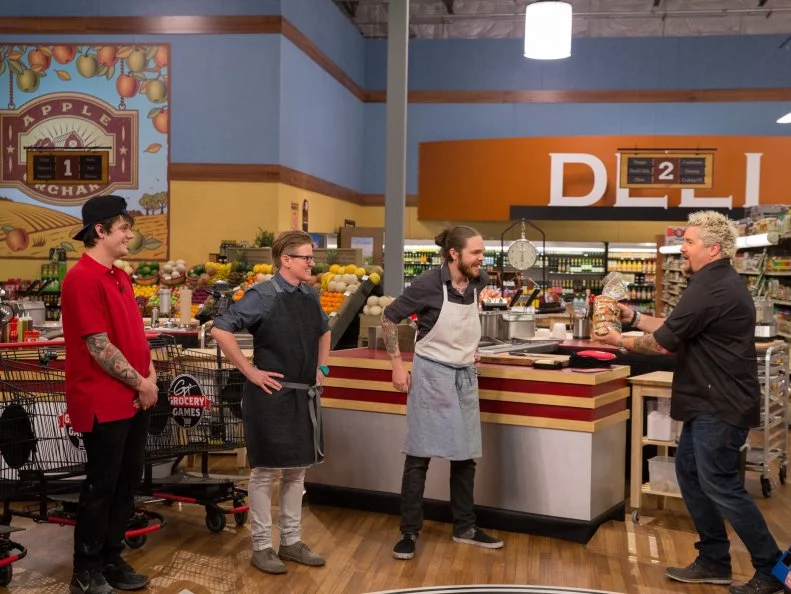 Host Guy Fieri prepares Chefs Jay Kean, Crista Luedtke, and Phillip Franklin Lee to shop during Game 2, Food Pyramid, as seen on Food Network's Guy's Grocery Games, Season 7.