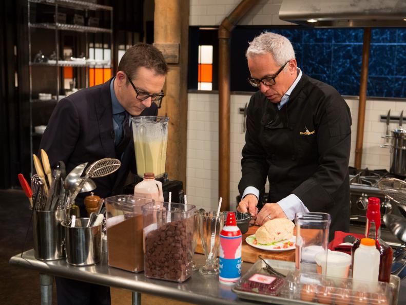 Chopped After Hours host Ted Allen checks in with chef Geoffrey Zakarian while he  works on his dish that must include the late night foods:a rice and cheese burrito, chocolate milk, canned whipped cream and apple pies, as seen on Food Network's Chopped After Hours, Season 22.