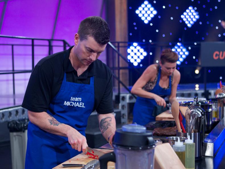 Cooks Bill Joerger (L) and Vanessa Craig of Team Michael during the first challenge where each team was given a different assignment. Team Alex was assigned Meat & Potatoes, Team Bobby was assigned Spaghetti & Meatballs, Team Michael was assigned Surf & Turf and Team Curtis was assigned Chicken & Waffles, as seen on Food Network's All-Star Academy, Season 1.