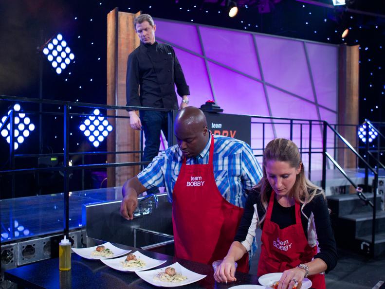 Chef Bobby Flay mentors Joseph Harris (L) and Angela George of Team Bobby during the first challenge where each team was given a different assignment. Team Alex was assigned Meat & Potatoes, Team Bobby was assigned Spaghetti & Meatballs, Team Michael was assigned Surf & Turf and Team Curtis was assigned Chicken & Waffles, as seen on Food Network's All-Star Academy, Season 1.