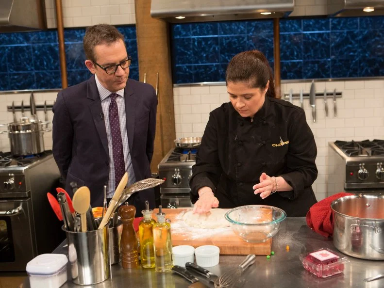 Chopped After Hours host Ted Allen chats with chef Alex Guarnaschelli as she works on her dish that must include: April fools day ingredients that are not what they seem. grilled cheese sandwiches = pound cake and frosting, tomato soup = strawberry puree, milk = buttermilk, peas and carrots = jelly beans, as seen on Food Network's chopped After Hours, season 23. as seen on Food Network's Chopped After Hours, Season 23.