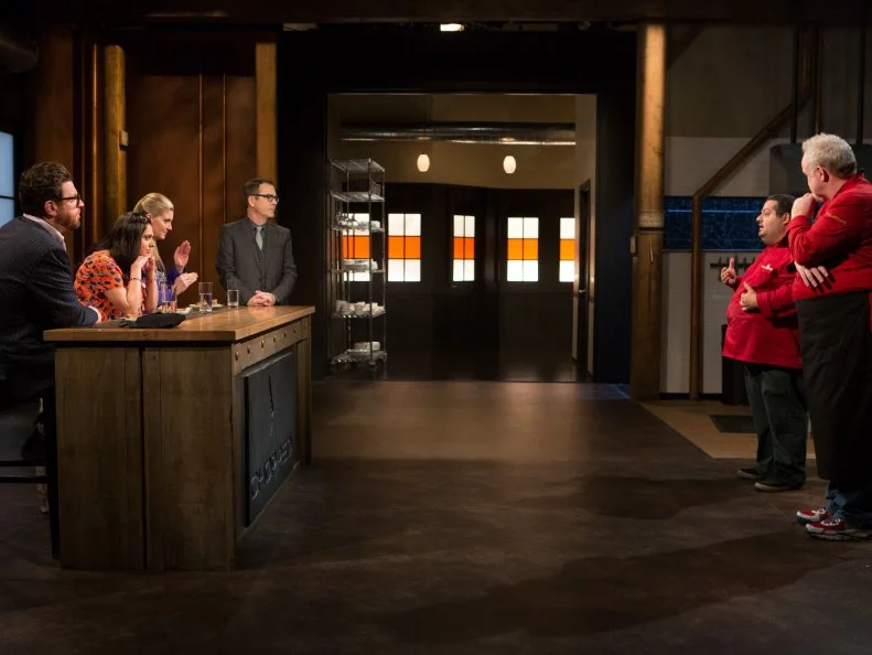 Chefs Eric Greenspan and Art Smith stand before host Ted Allen and judges: Scott Conant, Maneet Chauhan and Amanda Freitag after finishing working on their desserts that must have included: Maple smoked Cheddar cheese, almond flour, mayonnaise and datesfor Chopped $75,000 charity All-Stars competition, as seen on Food Network's Chopped, Season 24.