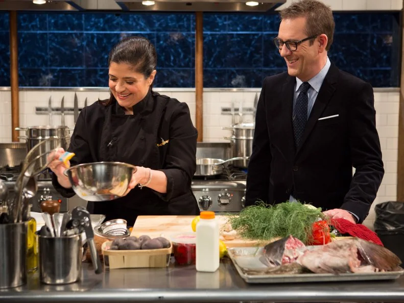 Chopped host Ted Allen checks in on chef Alex Guarnaschelli as she works on her appetizer made from the mystery basket ingredients from episode-24-07 (all star finale) are: fish carcass, calabrian chiles, tasso ham and purple potatoes, as seen on Food Networks Chopped, season 27 webisode