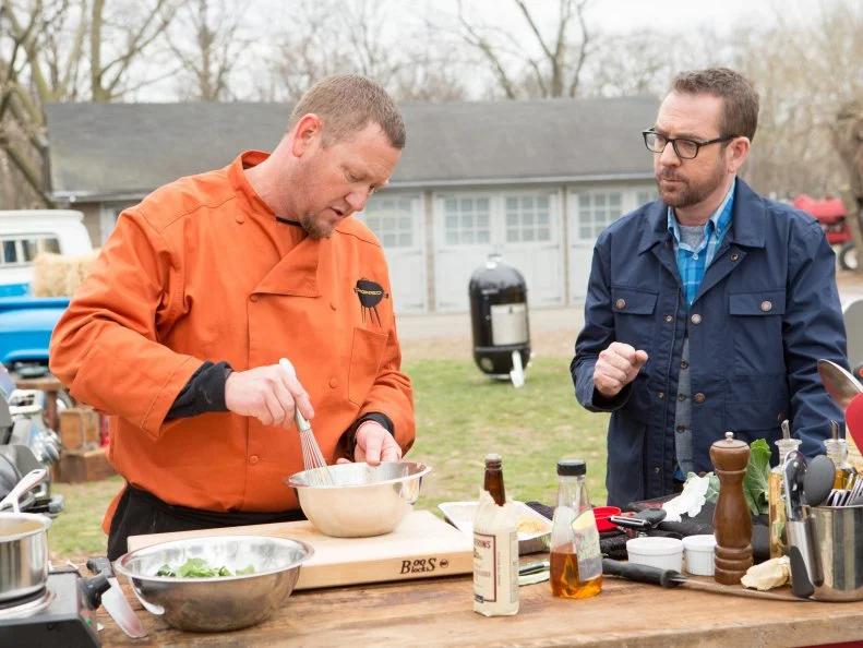 Chopped host Ted Allen checks in with Chef Stan Hays as he works on his entree that must include: rack of elk, Lea and Perrins worcestershire sauce, deviled eggs and collard greens, as seen on Food Network's Chopped, Grill Masters Special.