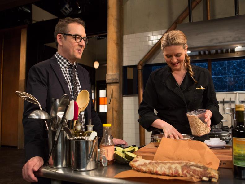 Chopped host Ted Allen chats with chef Frietag as she works on her dish that must include: North Carolina style bbq sauce, pork spare ribs, rainbow chard and avacados , as seen on Food Network's Chopped After Hours, Season 23.