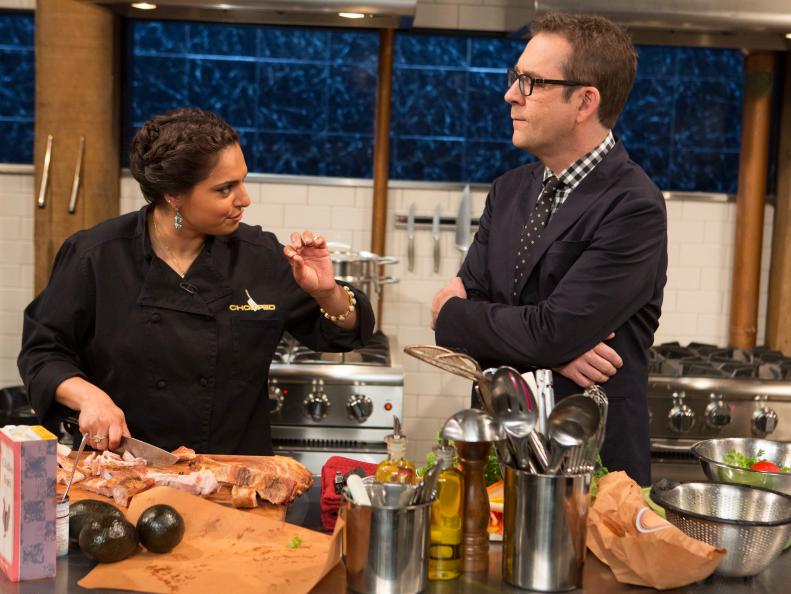 Chopped host Ted Allen chats with chef Maneet Chauhan while she works on her dish that must include: North Carolina style bbq sauce, pork spare ribs, rainbow chard and avacados , as seen on Food Network's Chopped After Hours, Season 23.
