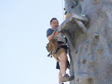 Judge Jet Tila climbing up the Round 2 sabotage element, Rock Wall Prep & Cook, as seen on Food Network's Cutthroat Kitchen, Camp Cutthroat Special.