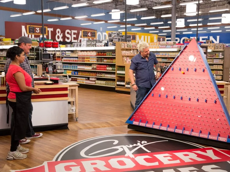 Host Guy Fieri introduces Game 3, Food Pyramid, to Judge Chefs Aarti Sequeira and Beau MacMillan, as seen on Food Network's Guy's Grocery Games, Season 7.