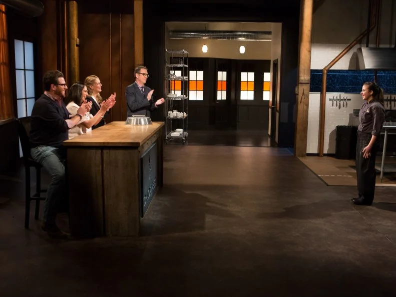 16 year old Yazmene Kaylani stands in front of Chopped host Ted Allen and judges: Scott Conant, Maneet Chauhan and Amanda Freitag moments after finding out she has become a Chopped Champion and will receive the first spot in the $25,000 tournament for Chopped Teen Week $25,000 tournament, as seen on Food Network's Chopped, Season 25.
