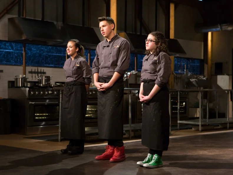 (L-R) Teens: Yazmene Kaylani (16), Theo Vicioso (17) and Anna Mindell (15) stand before Chopped host Ted Allen and judges: Scott Conant, Maneet Chauhan and Amanda Freitag to defend their work on their entrees that must include: hanger steak, lollipop kale, apple crisp and spray cheese for Chopped Teen Week $25,000 tournament, as seen on Food Network's Chopped, Season 25.