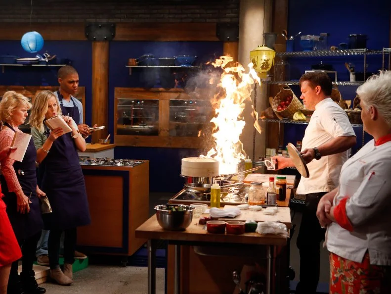 Co-Hosts Tyler Florence and Anne Burrell give a demonstration to the recruits before the Southeast Asian Street Food elimination challenge as seen on Food Network's Worst Cooks in America, Season 8.