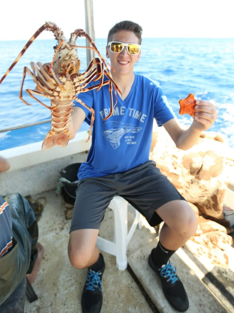 Portrait shot of Hunter Fieri holding up a lobster and a starfish in Crete, Greece on a boat in the Mediterranean sea as seen in Food Network's Guy's European Vacation episode 1.