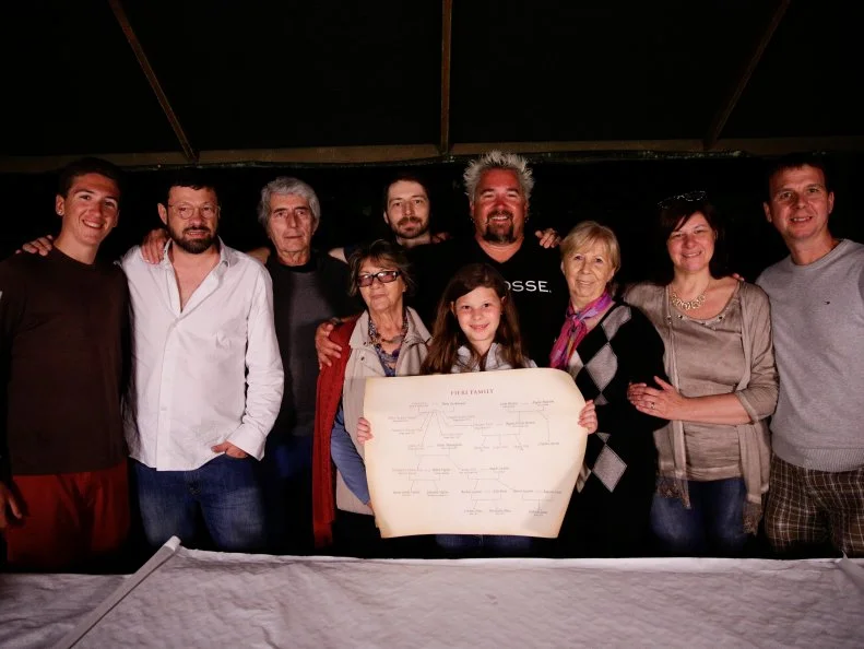 Portrait shot of Guy and Hunter Fieri with their family in Sesto Calende, Italy holding up a map of their family tree as seen on Food Network's Guy's European Vacation episode 2.