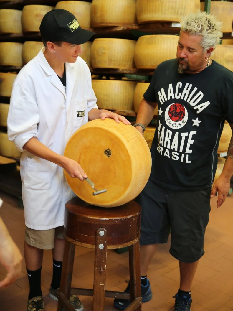 Hunter Fieri holding a Parmigiano Reggiano cheese wheel with Guy at the Consorzio del Formaggio Parmigiano Reggiano in Parma, Italy as seen on Food Network's Guy's European Vacation episode 3.