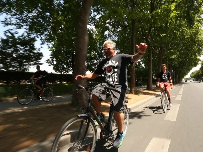 Guy and Hunter taking a bike tour around Arch de Triumph in Paris, France and Guy is riding hands free as seen on Food Network's Guy's European Vacation episode 4.