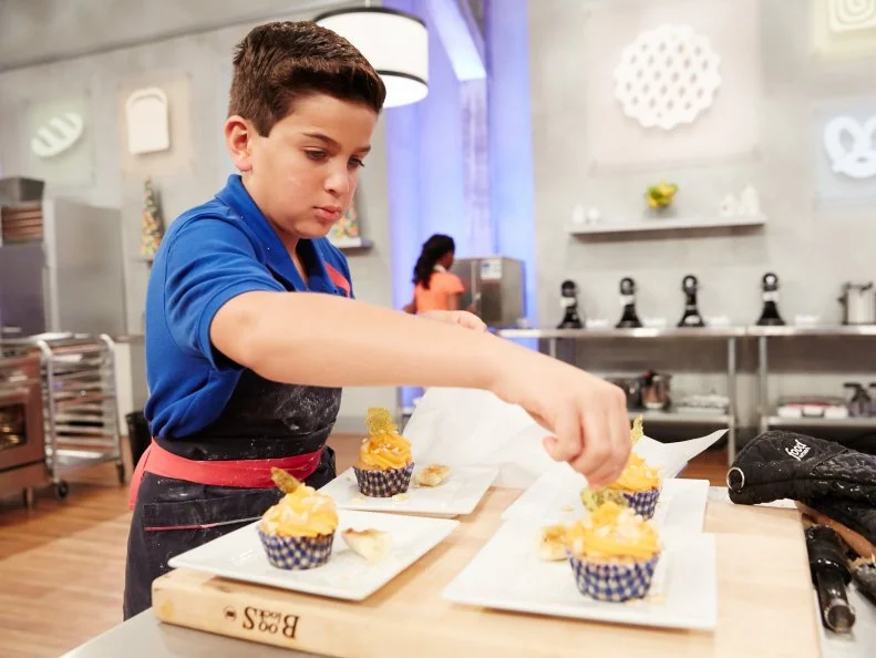 Contestant Matthew Merril preparing his dish, Banana Walnut Cupcake with Apricot Jam and Cream Cheese Frosting, for the challenge, Lunchbox Desserts, as seen on Food Network’s Kids Baking Championship, Season 2.