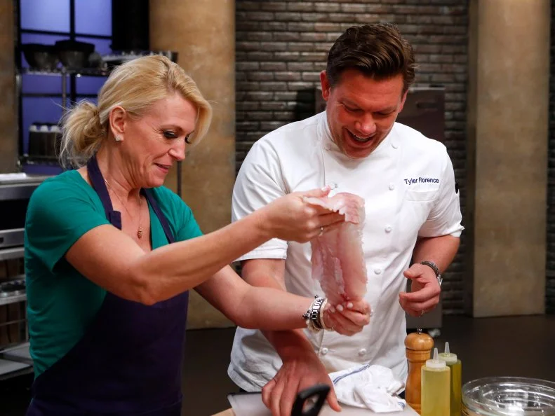 Host Tyler Florence checks in on blue team recruit Ginny Meerman as she prepares Fish and Chips during the elimination challenge as seen on Food Network's Worst Cooks in America, Season 8.