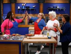 Mentors Anne Burrell and Rachael Ray look on as Nicole Sullivan of the red team and Loni Love of the blue team celebrate after completing a practice cook their finale menus, as seen on Food Network's Worst Cooks in America, Season 9.