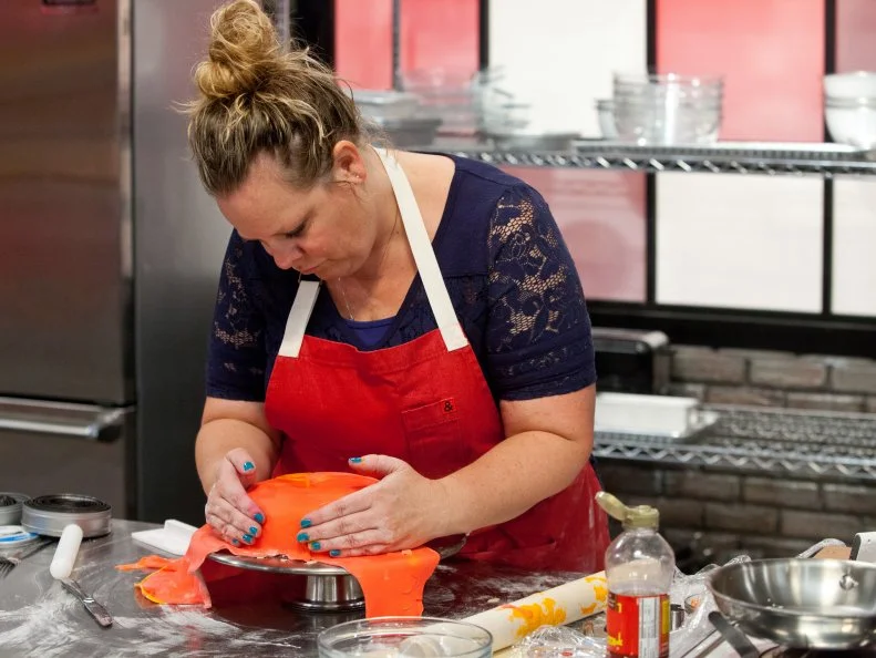 Contestant Stephanie Garcia works on layering and smoothing out the fondant layer over her birthday cake, as seen on Food Network's Worst Bakers In America, Season 1.