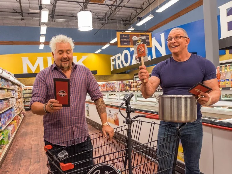Judge Robert Irvine happily holds up a 'Guy Fieri spatula', as seen on Food Network's Guy's Grocery Games, Season 11.
