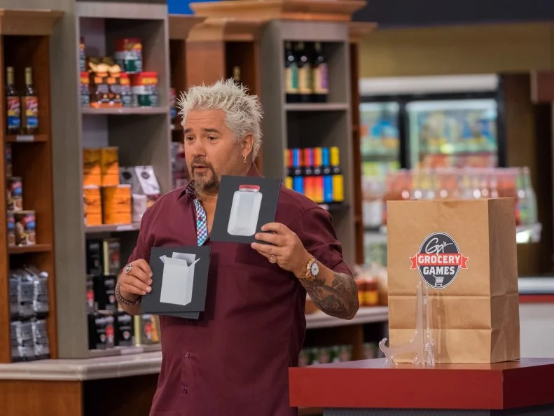 Host Guy Fieri holds up cards while he explains the next challenge, as seen on Food Network's Guy's Grocery Games, Season 11.