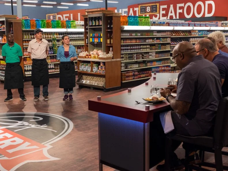 Contestants Andy Hyde, Alex Malmborg, and Samantha Mitchel watch as judges Richard Blais, Robert Irvine, and G.Garvin taste Samantha Mitchel's dish, as seen on Food Network's Guy's Grocery Games, Season 11.