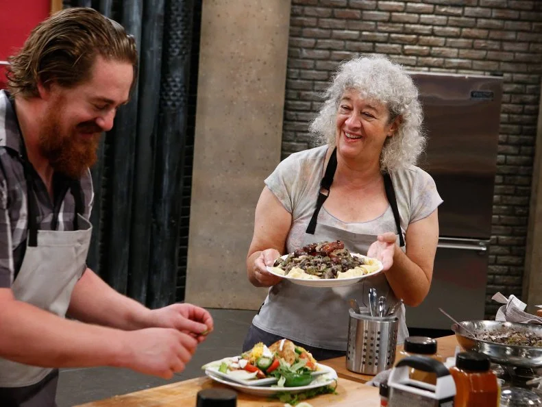 Jetta Ostrofsky offers her dish to Adam Cooke as they cook during the baseline challenge, as seen on Food Network's Worst Cooks in America, Season 10.