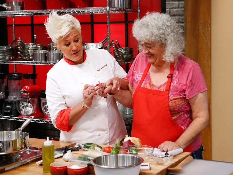 Mentor Anne Burrell helps Jetta Ostrofsky of the red team as she cooks during the main dish challenge, as seen on Food Network's Worst Cooks in America, Season 10.