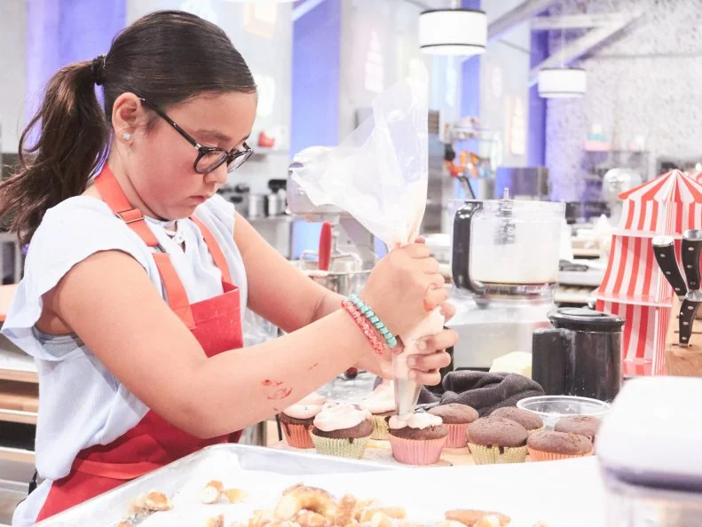 Contestant Keili Gorczyca preparing her Main Heat dish, Vanilla Tie Dye Cupcake with Deep Fried Pretzels and Vanilla Chocolate Sandwich Cookie Cream Buttercream, with the Pretzel Carnival Treat, as seen on Food Network's Kids Baking Championship, Season 3.