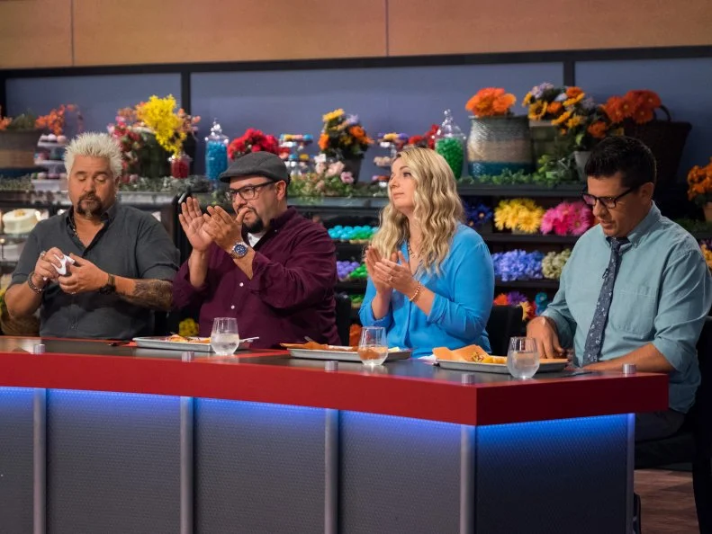 Host Guy Fieri and judges Carl Ruiz, Damaris and Troy Johnson clap for contestant Zane Caplansky's dish, as seen on Food Network's Guy's Grocery Games, Season 12.