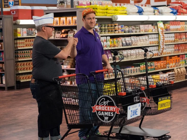 Contestants Zane Caplansky and Adam Gold prepare to play Regional Road Trip, as seen on Food Network's Guy's Grocery Games, Season 12.