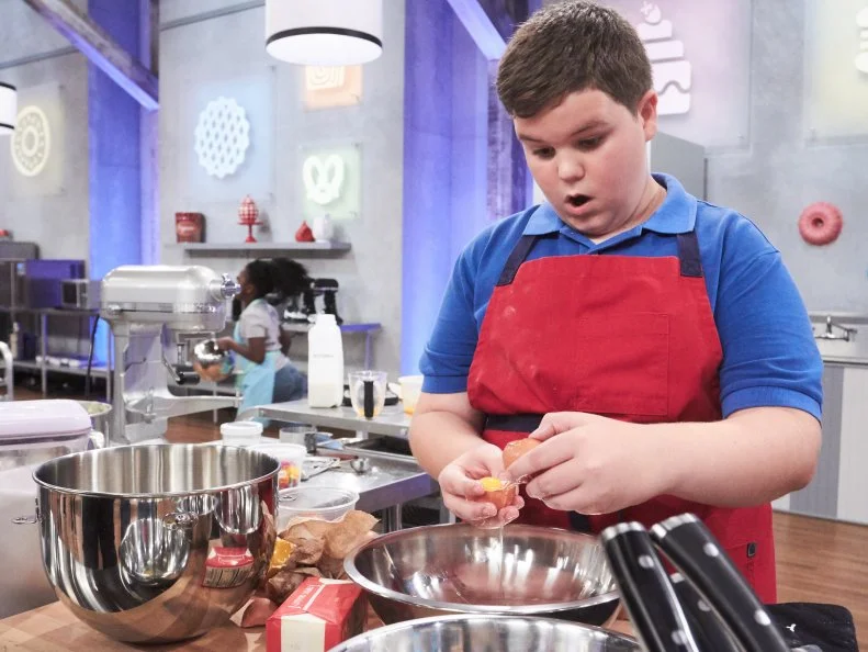 Contestant Aidan Berry preparing his Main Heat dish, Passion Fruit Cake with Banana Buttercream Frosting and Chocolate Cream Filled Baked Cookie Boulders, as seen on Food Network's Kids Baking Championship, Season 3.