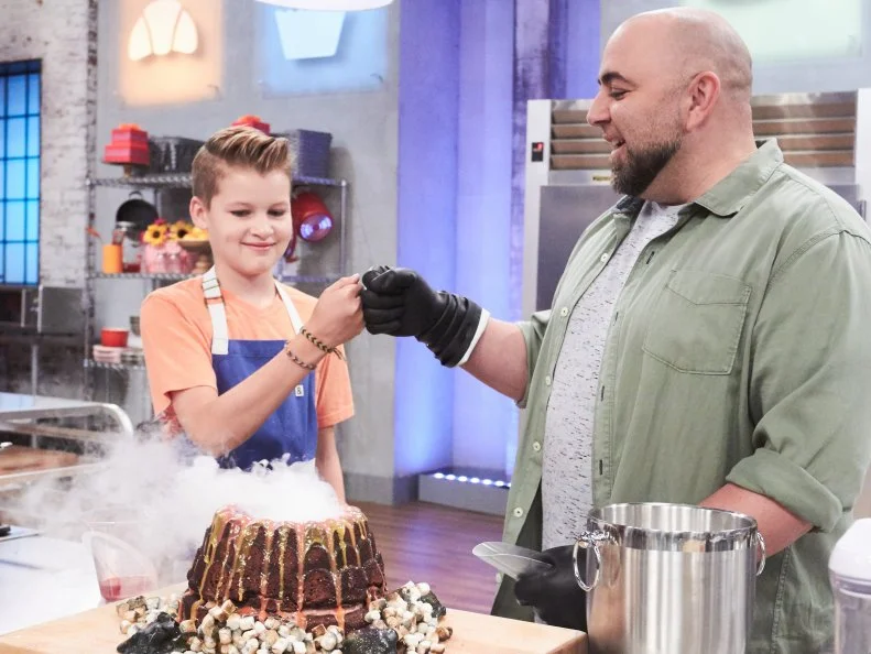 Host Duff Goldman helps contestant Cole Frederickson prepare his Main Heat dish, Chocolate Cinnamon Cake with Chocolate Strawberry Buttercream and Pecan Truffle Boulders, as seen on Food Network's Kids Baking Championship, Season 3.