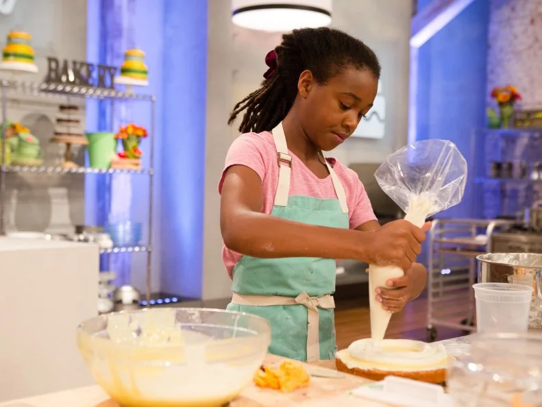 Contestant Yashimabet Sellassie pipes frosting onto her camping themed cake for the final challenge, "Spring Break Cakes", as seen on Food Network's Kids Baking Championship, Season 2.