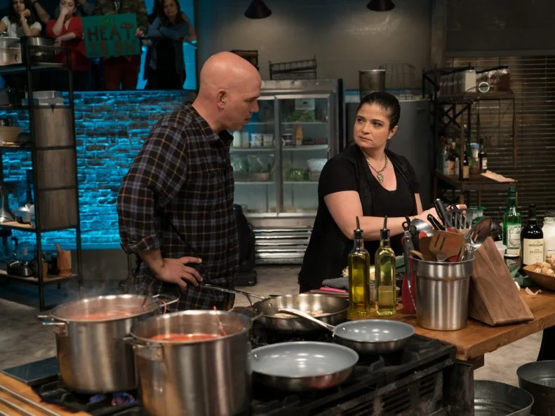 Guest judge Michael Symon checks in on contestant Alex Guarneschelli as she races to finish her Round 2 lobster newburg dish, as seen on Food Network's Beat Bobby Flay, Season 8.