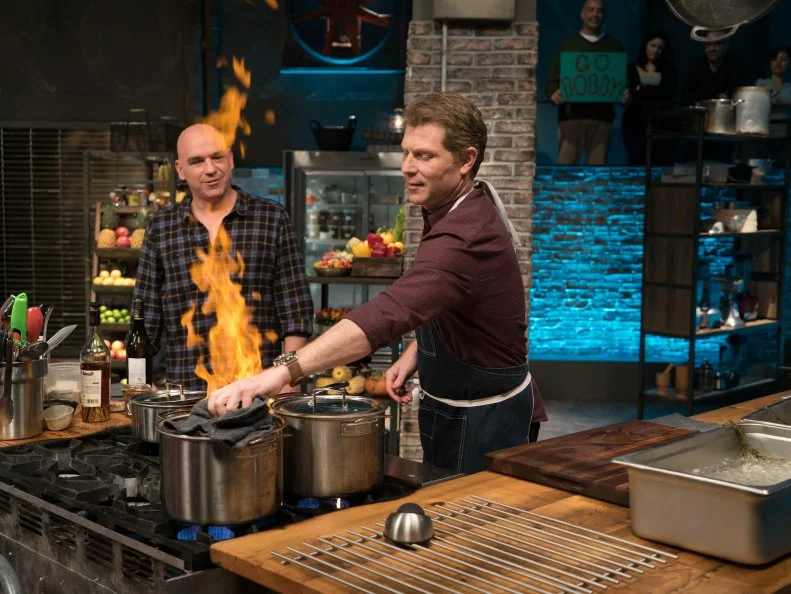 Guest judge Michael Symon checks in on host Bobby Flay as he races to finish his Round 2 lobster newburg dish, as seen on Food Network's Beat Bobby Flay, Season 8.