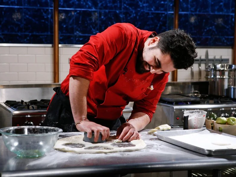 Chef Meny Vaknin cooks with curry cooking sauce, lady apples, coconut brittle and artichokes during the dessert round, as seen on Food Network's Chopped, Season 28.