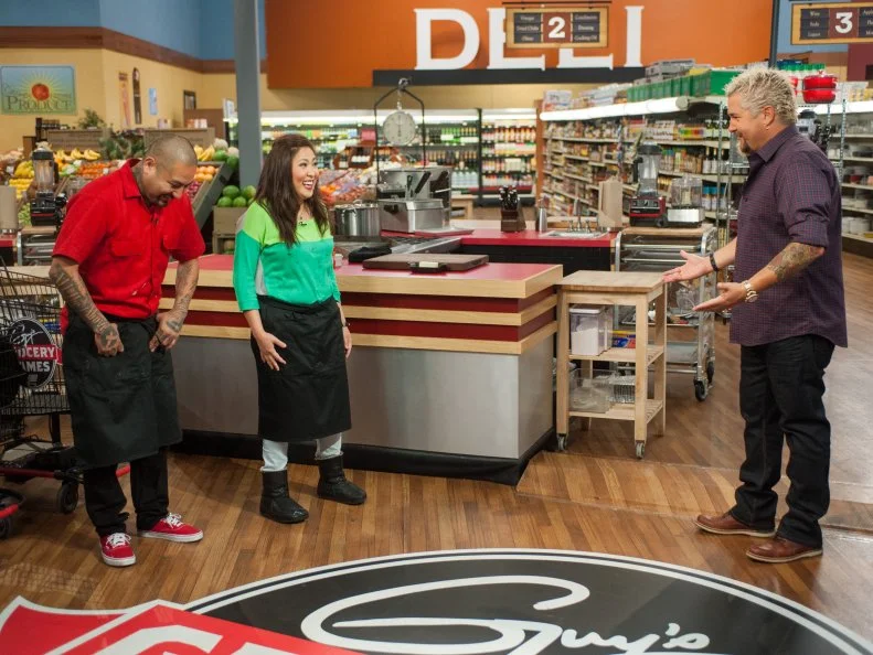 Host Guy Fieri explains the rules to contestant Chris Tzorin and Johanna Lawrence for the "2 in 1" competition, as seen on Food Network's Guy's Grocery Games, Season 9.