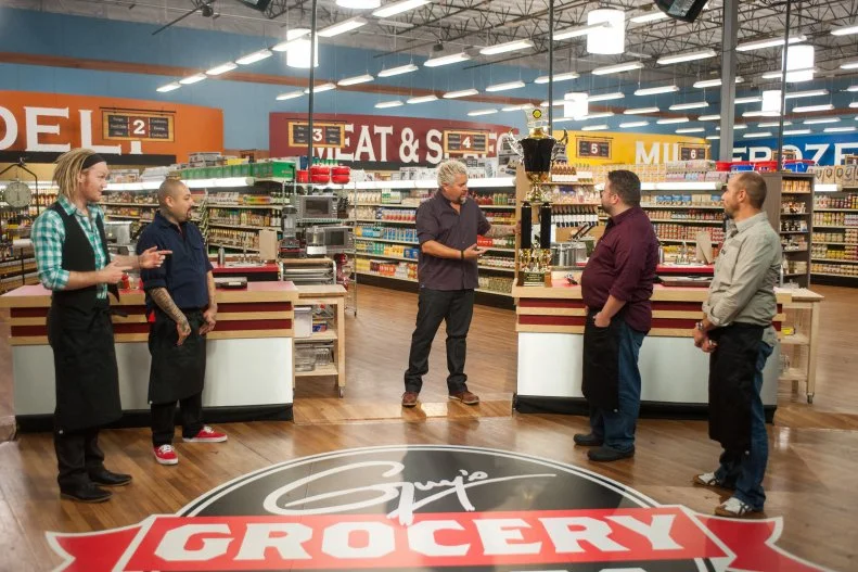 Host Guy Fieri welcomes contestants Chase Meneely, Chris Tzorin, Robbie Jester and Stephane Meloni, as seen on Food Network's Guy's Grocery Games, Season 9.