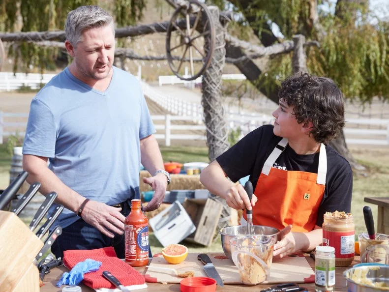 Guest Judge Tim Love with contestant LJ Ruth, as he prepares his dish for the Chicken BBQ Challenge, as seen on Food Network’s Kids BBQ Challenge Season 1.