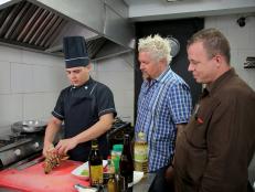 Host Guy Fieri and owner Gilberto Reina observe as chef Felix Cruz prepares lobster in the kitchen of El Figaro in Havana, Cuba as seen on Food Network's Diners, Drive-Ins, and Dives episode 2411.