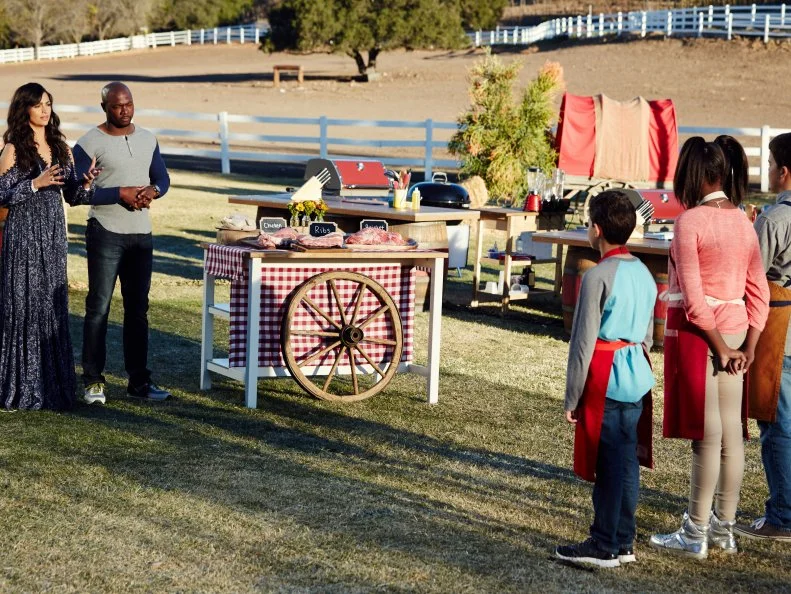 Hosts Eddie Jackson and Camila Alves with Contestants Tyler Zager, Paris Hale, and Carter Hull at the start of the finale, as seen on Food Network’s Kids BBQ Challenge Season 1.