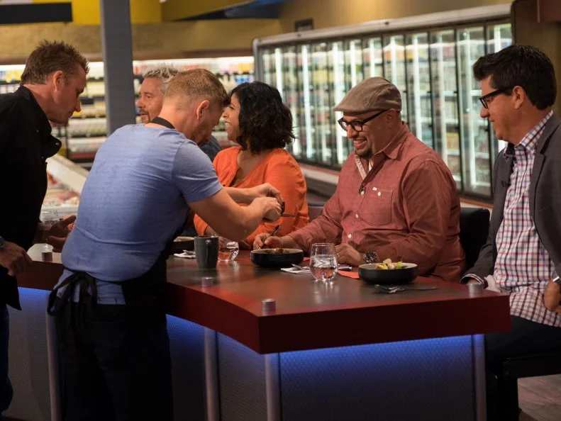 Contestant Marc Murphy and host Guy Fieri look on as contestant Richard Blais makes a late addition to his dish for judges Aarti Sequeira, Carl Ruiz and Troy Johnson, as seen on Food Network's Guy's Grocery Games, Season 10.