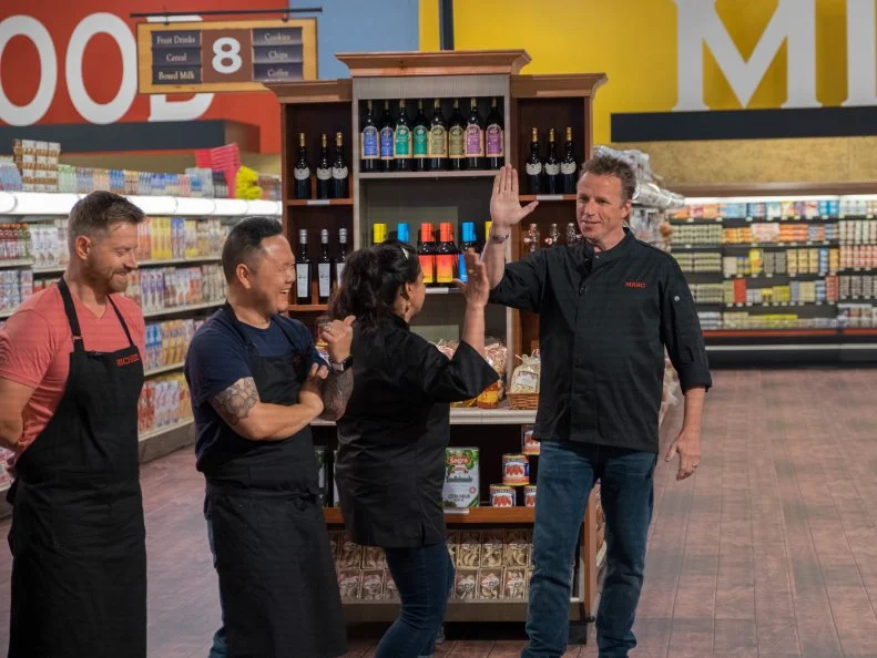 Contestants Richard Blais and Jet Tila look on as Maneet Chauhan and Marc Murphy high five, as seen on Food Network's Guy's Grocery Games, Season 10.