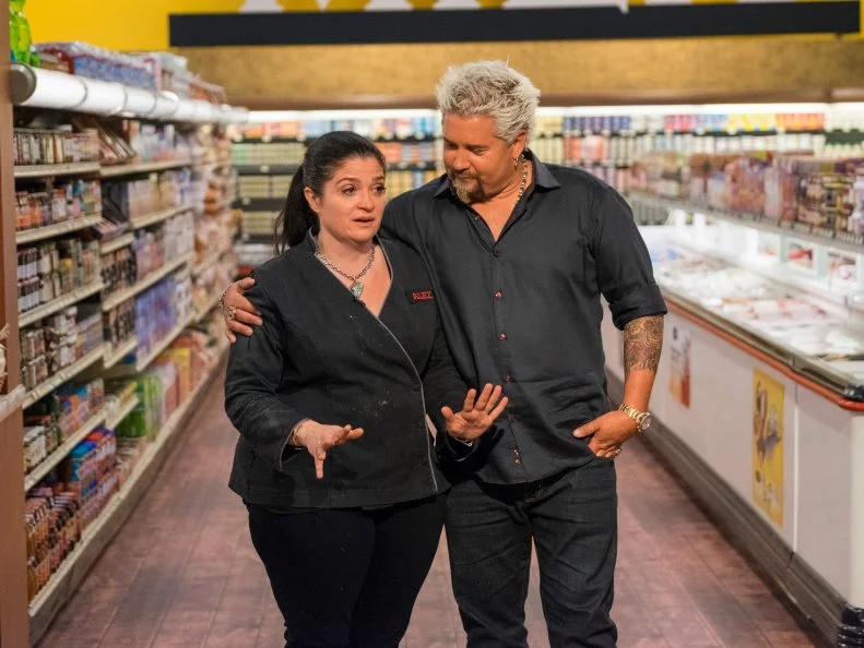 Host Guy Fieri congratulates a very shocked Alex Guarnaschelli, the new winner of Guy's Superstar Games, as seen on Food Network's Guy's Grocery Games, Season 10.