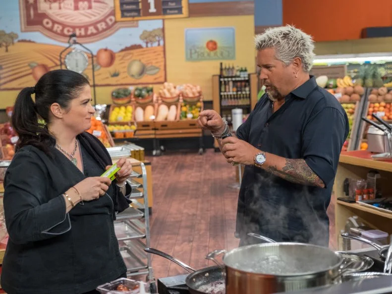 Host Guy Fieri checks on contestant Aarti Sequeira, as seen on Food Network's Guy's Grocery Games, Season 10.