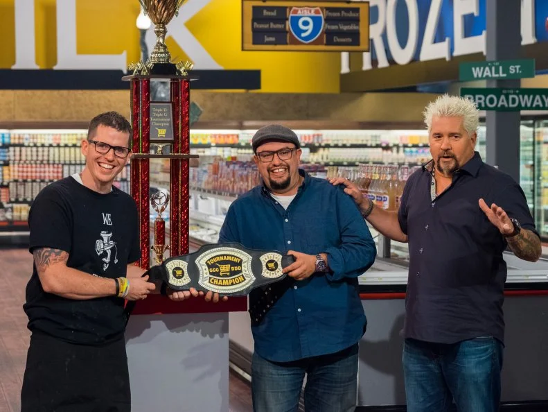Contestant Bobby Marcotte, Host Guy Fieri, and Judge Carl Ruiz pose with the GGG DDD Tournament Championship Belt, as seen on Food Network's Guy's Grocery Games, Season 12.