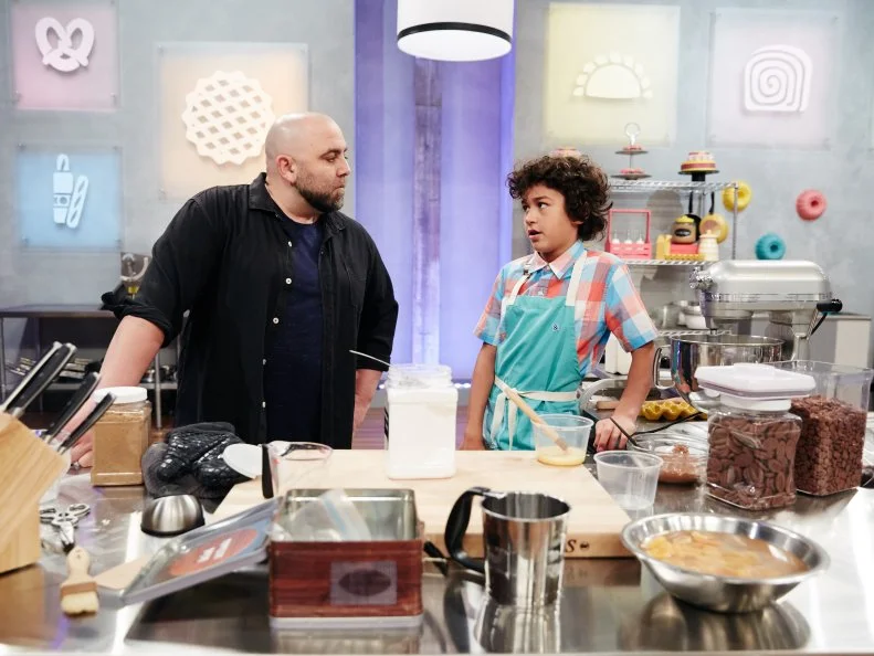Host Duff Goldman watches contestant Justice Faustina preparing his Main Heat dish, Black Forest Éclair with Chocolate Cherry Whipped Cream and Apricot Ganache, as seen on Food Network's Kids Baking Championship, Season 3.